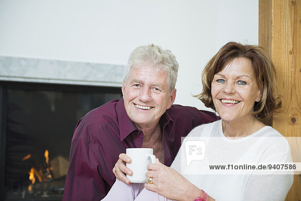 Portrait of senior couple sitting in front of fireplace  smiling
