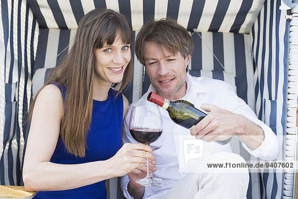 Couple having vine in roofed wicker beach chair  smiling