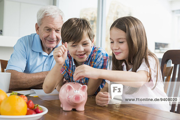 Two children and grandfather with piggy bank