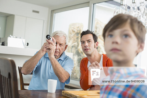 Grandfather looking through telescope watched by father and grandson