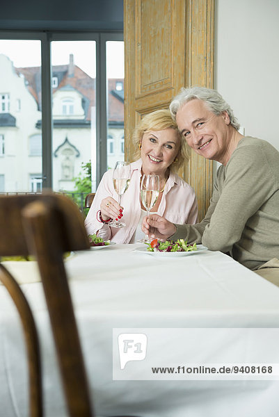 Portrait of mature couple sitting at table with sprinkling wine  smiling