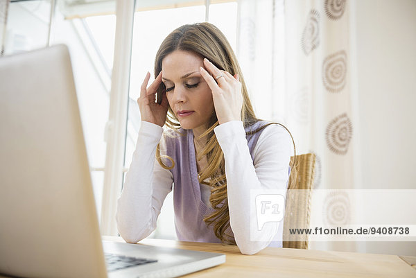 Serious woman with head in hand using laptop at home