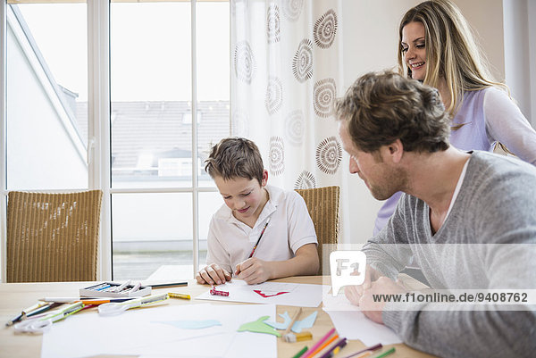 Boy drawing a picture with parents at table