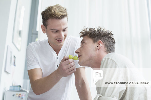 Young man feeding grapes to another man  smiling