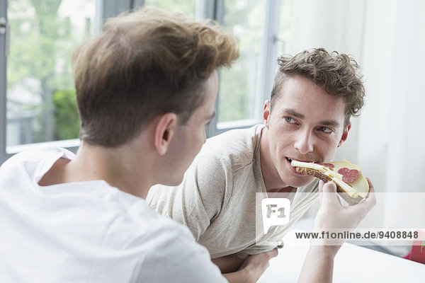 Young man feeding bread to another man