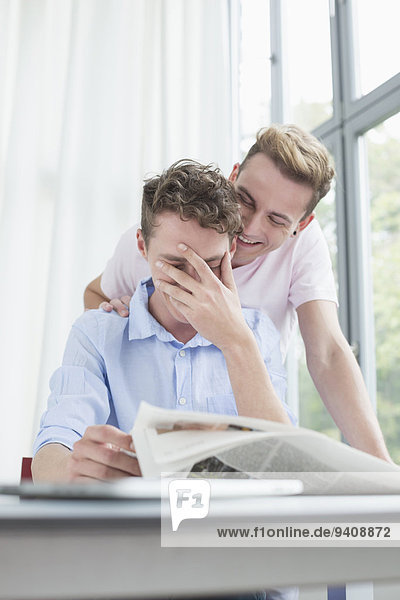 Homosexual couple smiling about newspaper
