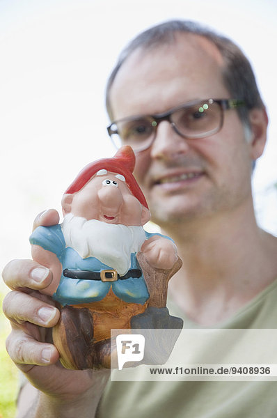Mature man holding garden gnome  smiling  portrait