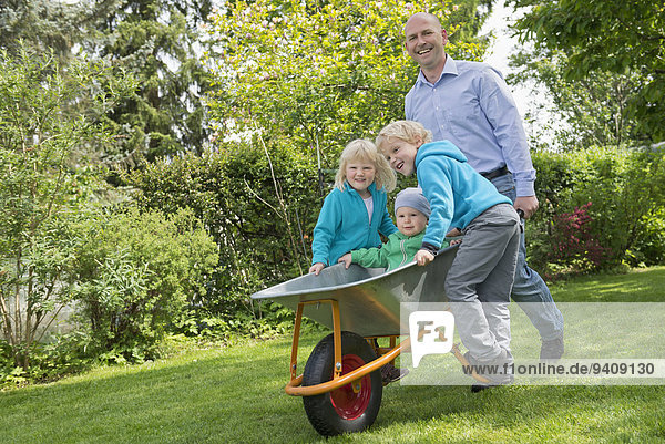 Father in garden pushing kids in wheelbarrow