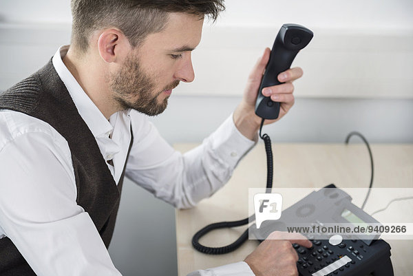 Manager in office dialing landline telephone