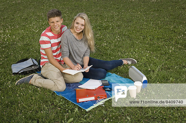 Portrait of teenage couple doing homework in park  smiling