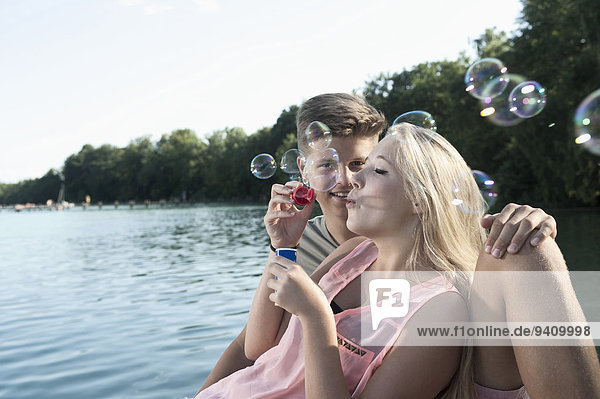 Teenage couple blowing soap bubbles on a jetty at lake