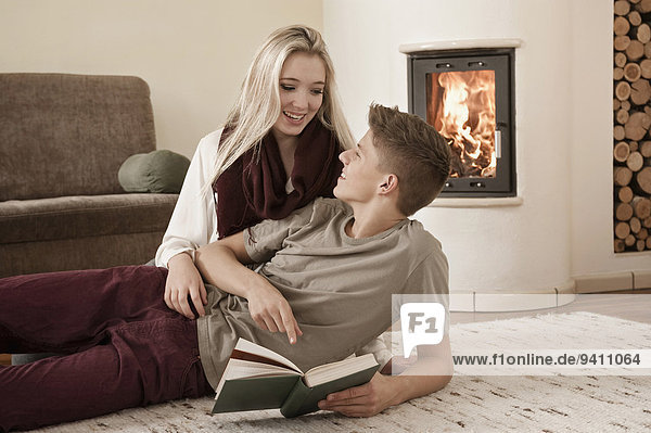 Teenage couple with book lying on carpet