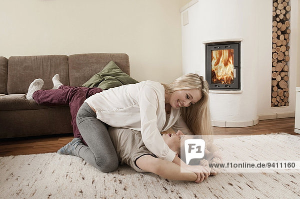 Teenage couple playfighting on carpet in front of fireside