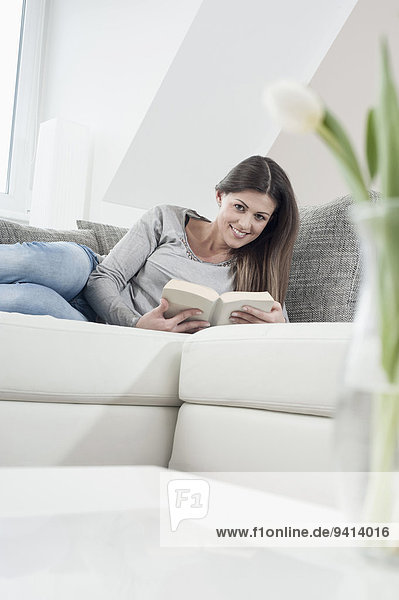 Smiling young woman reading a book on her couch at home