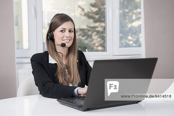 Portrait of young business woman with laptop and headset