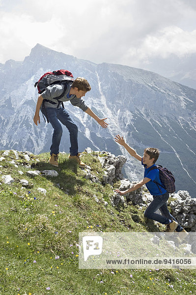 Teenage boys helping friend climbing in mountains