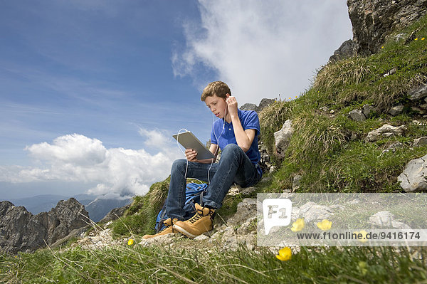 Teenage boy using iPad in mountain landscape