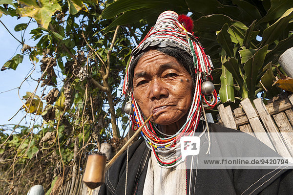 Traditionally dressed elderly woman from the Akha people hill tribe ethnic minority smoking a pipe portrait Chiang Rai Province Northern Thailand Thailand