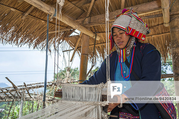 Traditionally dressed woman from the Akha people hill tribe ethnic minority working on a loom Chiang Rai Province Northern Thailand Thailand