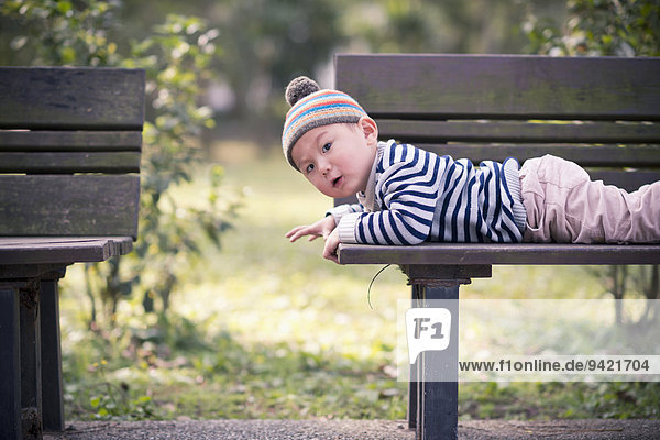 Kind liegt auf einer Parkbank  bei der Erkundung der Umgebung