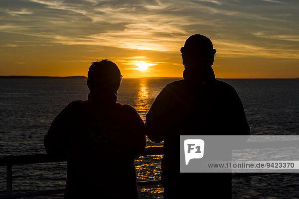 Paar an der Reling eines Schiffes beobachtet den Sonnenuntergang im Nordatlantik  Küste vor Thurso  Schottland  Großbritannien