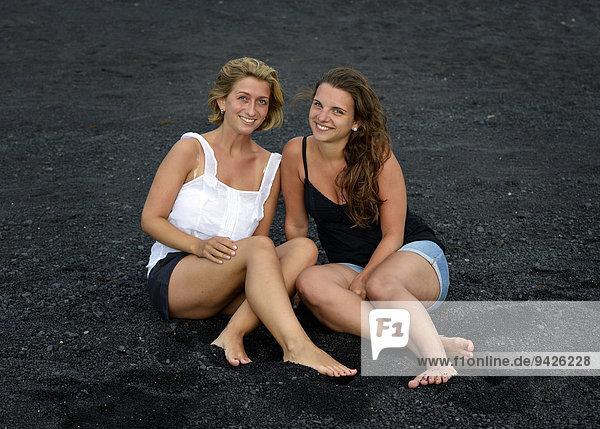 Two young women  girlfriends  on a black lava beach  Lanzarote  Canary Islands  Spain