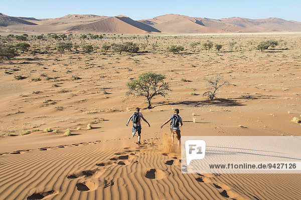 Two teens running down a dune  Sossusvlei  Namib Desert  Namibia
