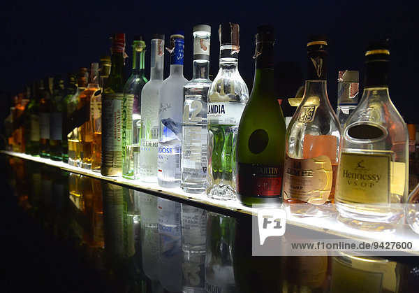 Flaschen mit diversen Spirituosen in einer Reihe spiegeln sich in Glasplatte