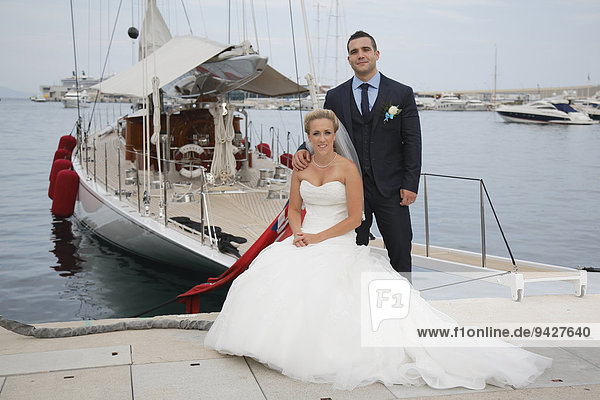 Bride and groom posing in front of a yacht in a marina