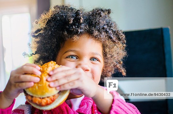 Portrait of cute girl eating hamburger in kitchen
