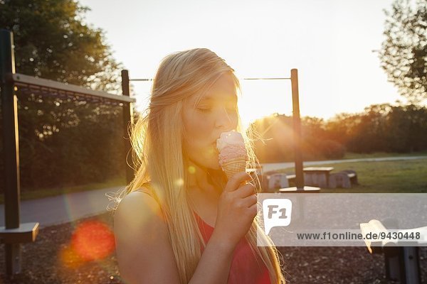 Junge Frau beim Eis essen im Park bei Sonnenuntergang