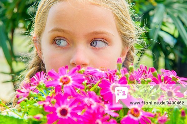 Nahaufnahme Porträt eines Mädchens  das seitlich hinter rosa Blumen schaut.