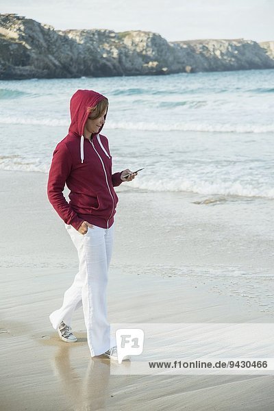 Mature woman reading text message on smartphone whilst strolling on beach  Camaret-sur-mer  Brittany  France