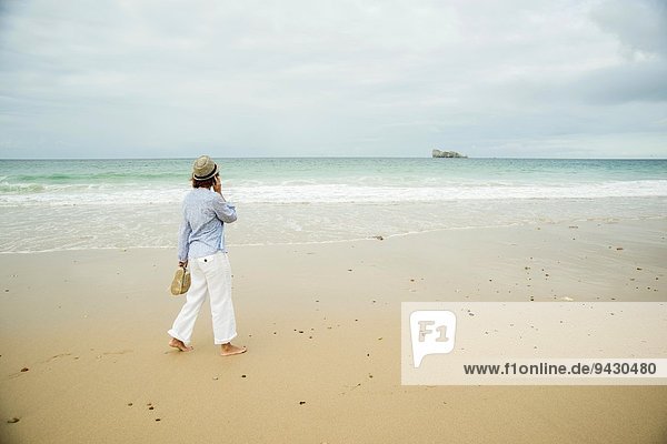 Reife Frau  die am Strand spazieren geht und mit dem Smartphone chattet  Camaret-sur-mer  Bretagne  Frankreich