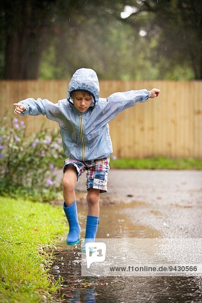 Junge in Gummistiefeln springend in der Regenpfütze