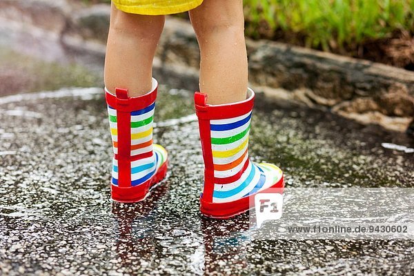 Beine des Mädchens in Gummistiefeln in Regenpfütze stehend