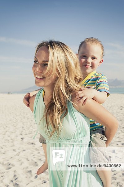 Mittlere erwachsene Mutter schenkt jungen Sohn Huckepack am Strand  Kapstadt  Westkap  Südafrika