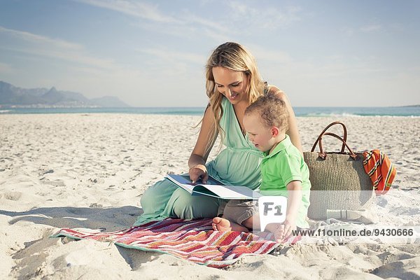 Mittlere erwachsene Mutter beim Lesen mit jungem Sohn am Strand  Kapstadt  Westkap  Südafrika