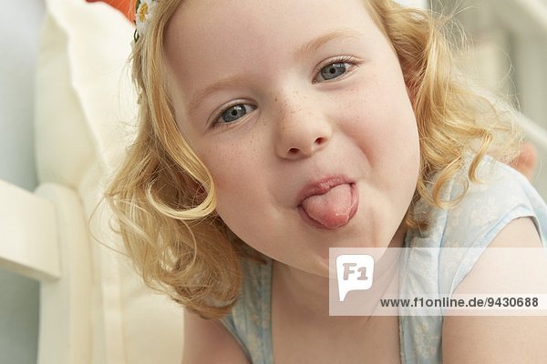 Portrait of girl lying on seat sticking tongue out