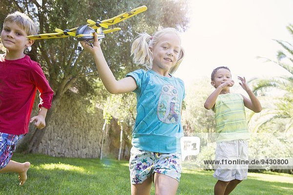 Three children in garden running with toy airplane