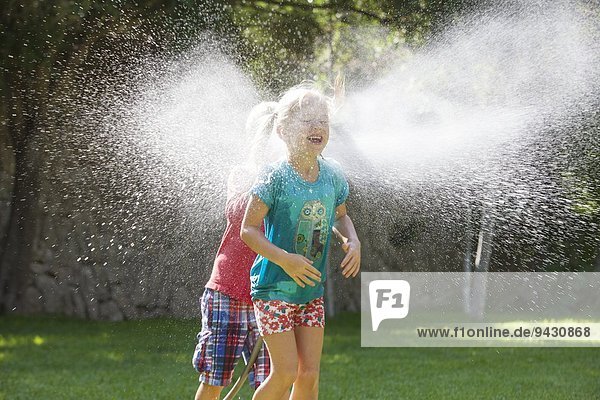 Boy chasing girl in garden with water sprinkler