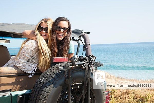 Portrait of two young women leaning out of jeep at coast  Malibu  California  USA