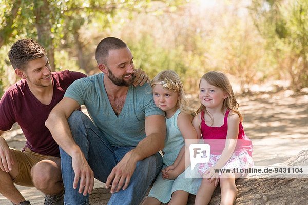 Male couple sitting on riverbank with two daughters