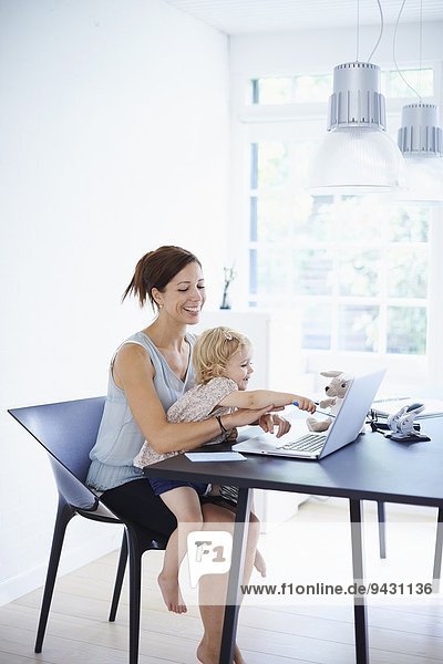 Mid adult woman using laptop with toddler daughter on her lap