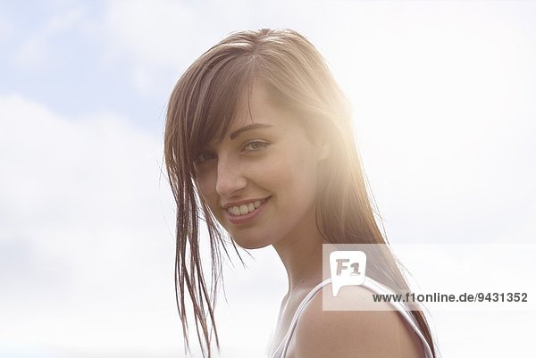 Porträt einer jungen Frau  die unter hellem Sonnenlicht lächelt.