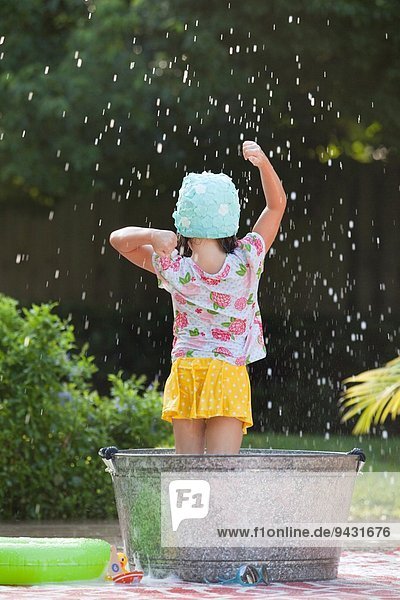 Rear view of girl standing in bubble bath in garden splashing soap bubbles