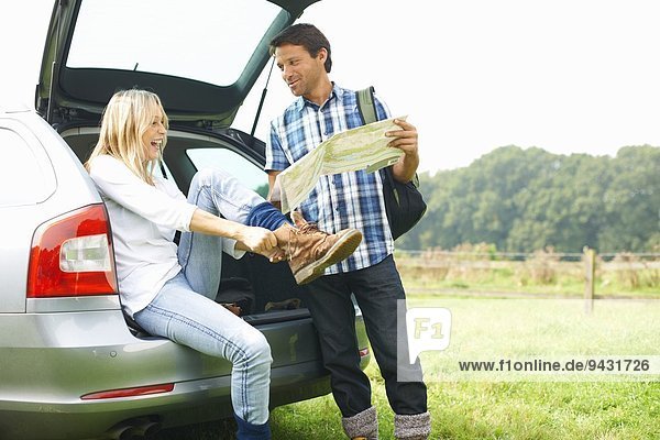 Couple at rear of car map reading preparing for walk