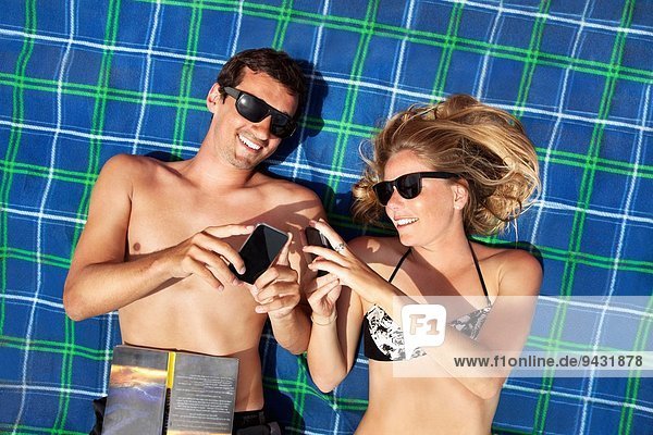 Junges Paar  das mit Smartphones auf dem Strandtuch liegt