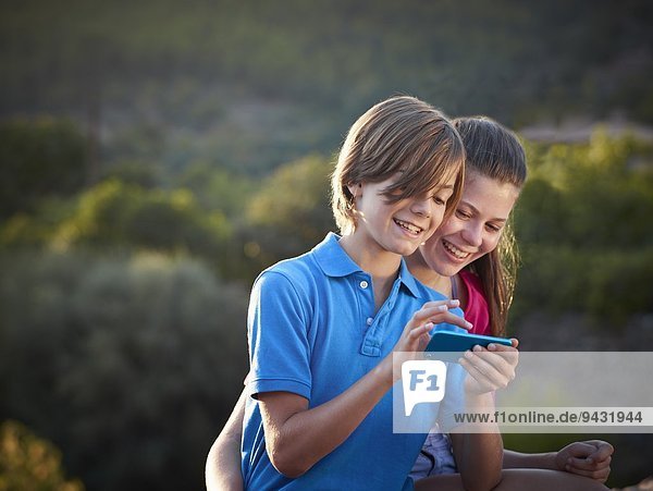 Bruder und jugendliche Schwester mit Touchscreen auf dem Smartphone,  Mallorca,  Spanien