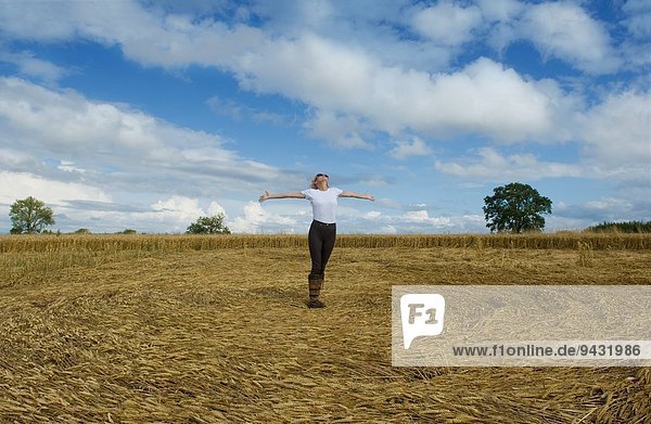 Reife Bäuerin feiert mit offenen Armen im geernteten Weizenfeld